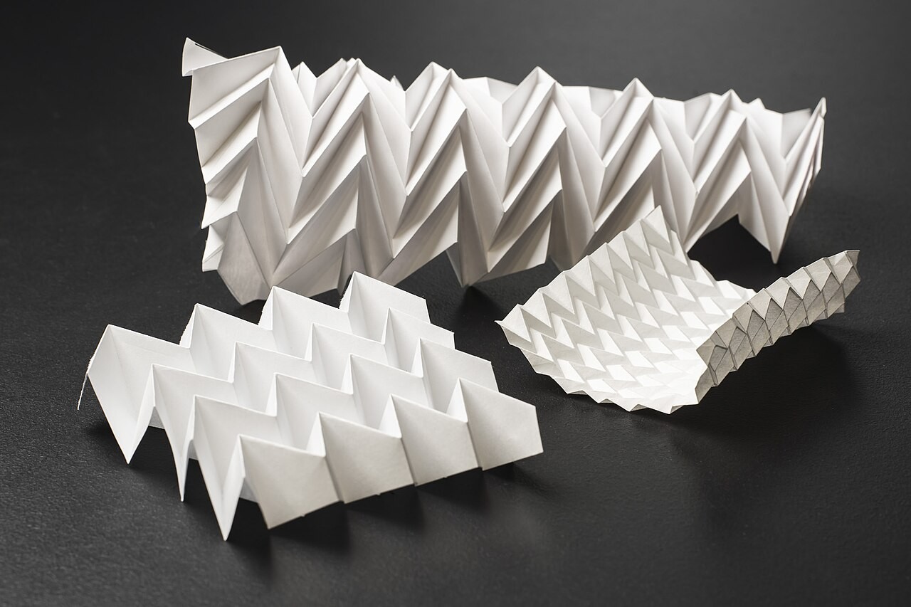Paper Miura-ori tessellations illustrate folding geometry. These are not the metal modules or sculpture tested by MIT.